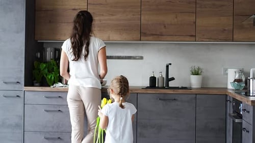 Girl Gives Flowers to Smiling Woman in Kitchen