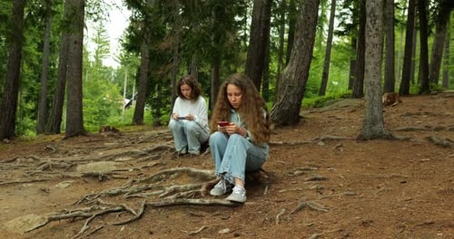 Two Teenage Schoolgirls Complete Assignments on Phones Amidst Forest Backdrop