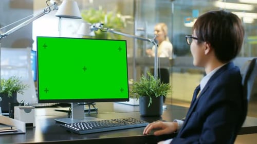 In the Office Businessman Makes Video Call on Personal Computer with Mock-up Green Screen.