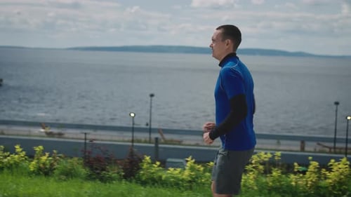 Ein junger, athletisch gebauter junger Mann läuft einen gut gepflegten Damm entlang — Workout, um fit zu bleiben und
