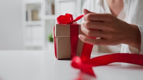 Woman Unties Ribbon on Small Wrapped Gift
