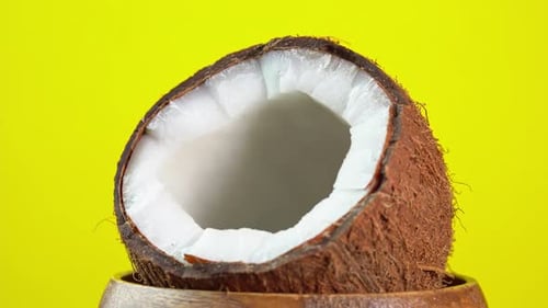 Coconut rotates on a yellow background in a wooden bowl. Cracked fresh coconut with splashing milk