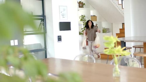 Mujer afroamericana que llega a casa con comida, sostiene dos bolsas con un bolso, bolsas de equilibrio