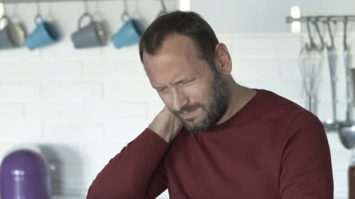 Man Massaging Stiff Neck at Kitchen Counter
