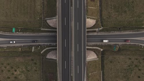 A top-down aerial view of a highway intersection with an overpass crossing above a main road.