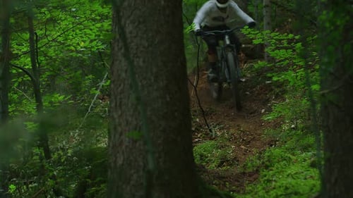 A mountain biker is riding down a trail in a forest very fast
