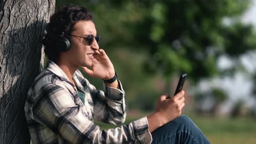 Arabic Man Relaxing Listening Music Smartphone App in Headphones Outdoor Summer Sunny Garden Park