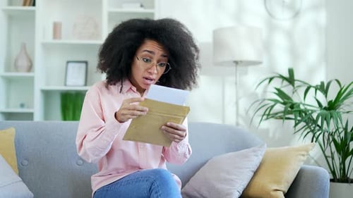Woman Reads Letter with Shocked Expression on Couch