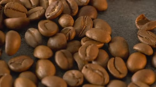 Roasted coffee beans poured on dark textured table, macro close up background, copy space.