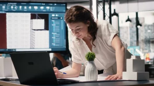 Woman Real Estate Engineer Reviews City Planning Blueprints on Laptop
