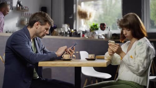 A Man and a Woman are Texting on the Phones on a Date in a Cafe
