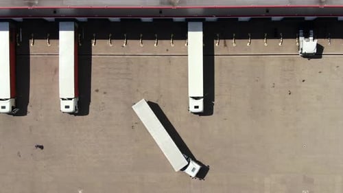 Semi truck with cargo trailer is travelling along a parking lot of a warehouse in the logistics park