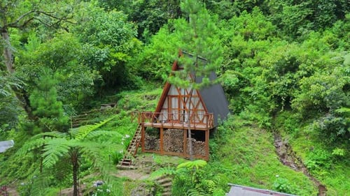 A-frame wooden cabin nestled in a lush tropical forest hillside
