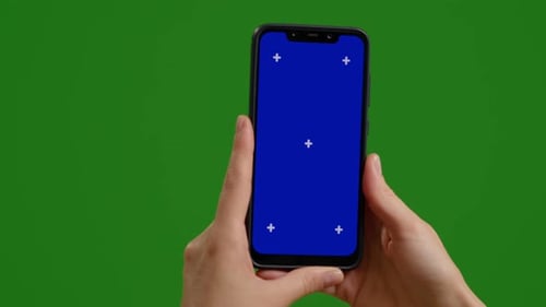 Woman holds blue chroma key screen device vertically with fingers on green background.