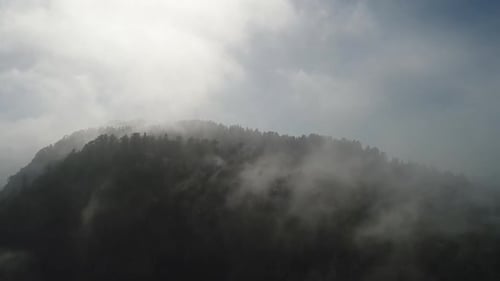 Slow moving drone shot of fog rolling over a mountain top.