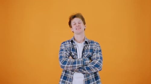 A Young Man in a Plaid Shirt Stands Against an Orange Background Possibly in a Studio Smiling