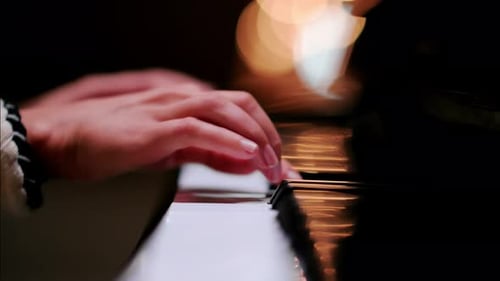 Close up of a woman's hands playing the piano with blurry lights on the background