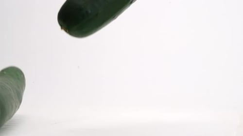 Close up of fresh green whole cucumbers bouncing on white table top in slow motion