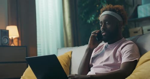 Young Man on Couch Using Laptop and Phone