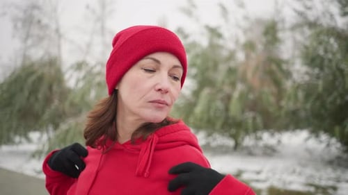 Woman in Red Hoodie Performing Shoulder Stretch Outdoors in Snowy Winter Park