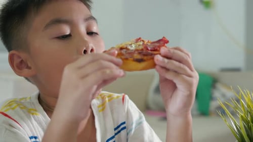Joyeux petit garçon asiatique de 5 ans assis en train de manger une énorme pizza sur la table à la maison