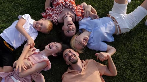 A Big Happy Family Lies on a Green Lawn in a Circle and Laughs Top View