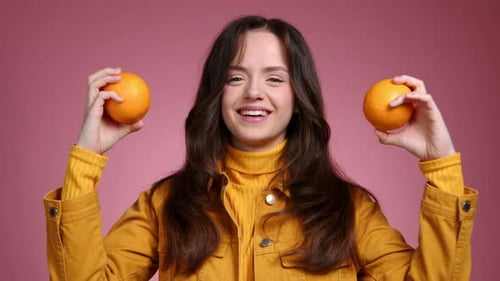 Woman Holds and Smells Two Oranges in Studio