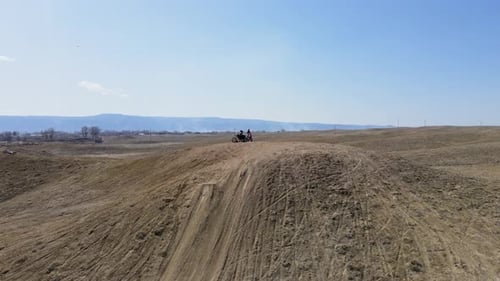 A spectacular, fast-paced drone shot of two motocross riders preparing to hit a big hill jump, in th