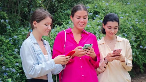 Young Women Friends Using Phones Together Outdoors