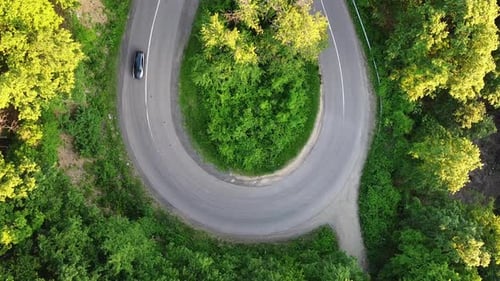 Aerial View of a Car Passing by on a Curly Road at a Forest during Summer
