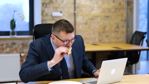 Man Eating Lunch While Working on Laptop