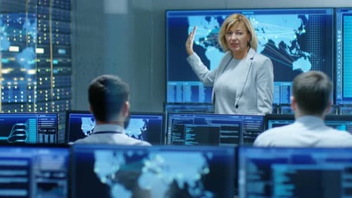 In the System Monitoring Room Senior Female Technician Holds Briefing for Operators, Showing them I