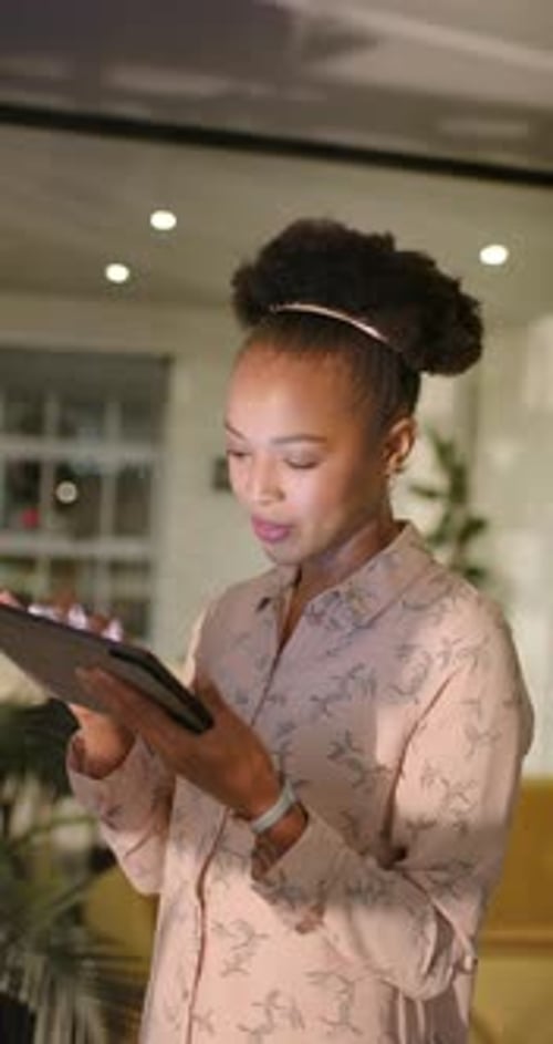 Vertical video: Using tablet, African American businesswoman working late in office