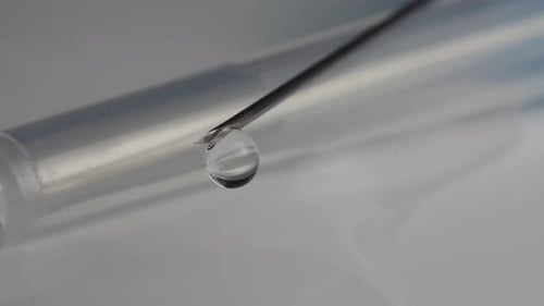 A medical syringe with a vaccine dripping from a needle. Reflection in a drop. Close-up.