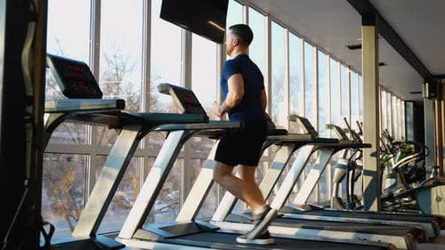 Man Jogging on Treadmill in Sunny Gym