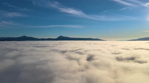 Aerial View of Yellow Sunset Over White Puffy Clouds with Distant Mountains on Horizon
