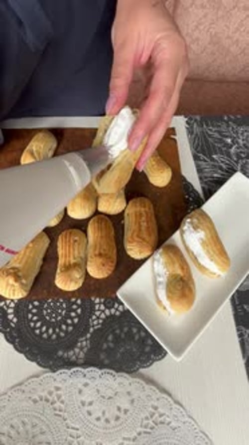 Eine Frau füllt Eclairs mit Sahne und legt sie auf einen Teller. Vertikales Video