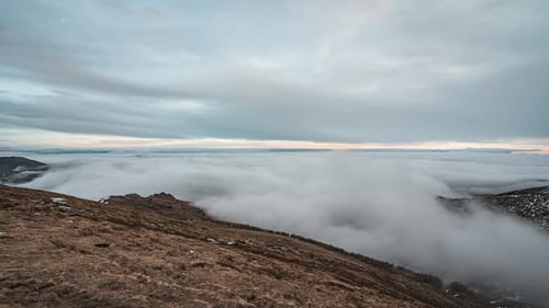 Expansive clouds roll over a rugged peak during a serene, wide-angled timelapse shot