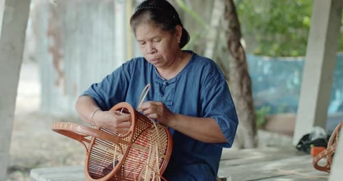 Une fermière thaïlandaise souriante tisse un panier avec des motifs d'art thaïlandais traditionnels
