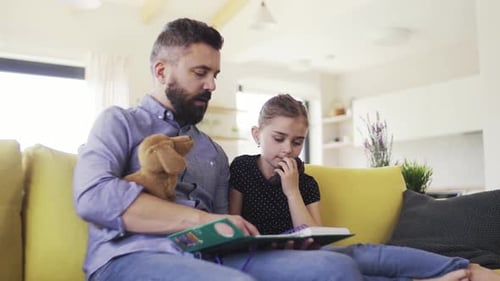 Man reading book to young girl on sofa