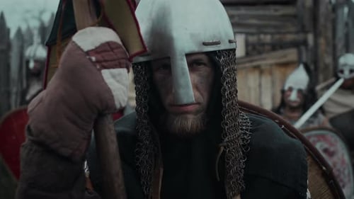 Portrait of Weary Young Medieval Guard in Helmet Leaning on Spear by Gate