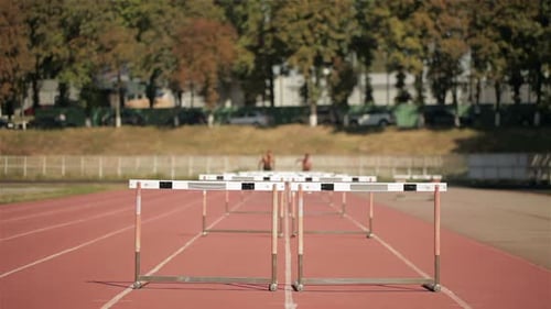 Two Athlets Run on Short Distance with Hurdles at the Stadium
