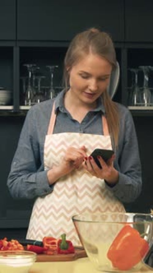 Young Woman in Kitchen Looking at Smartphone