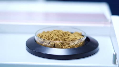 In a lab setting, a cylindrical vessel is placed within an enigmatic apparatus, holding a mound of b