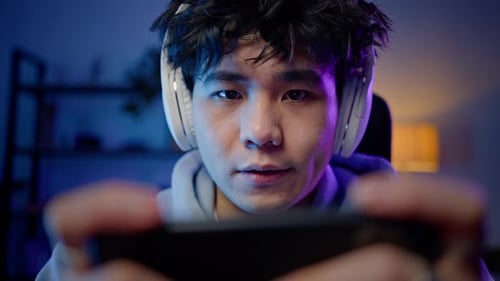 Young Man Playing Mobile Game Indoors at Night