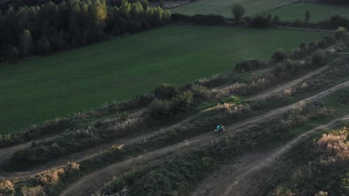 Aerial top down follow cam of a motorcyclist riding dirt bike on a winding dirt path through a rugge