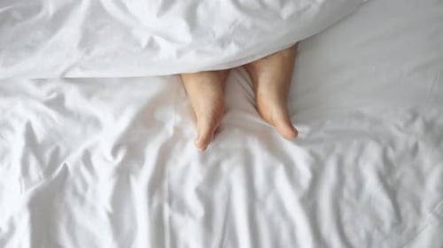 Bare Feet Under White Sheets in Bed