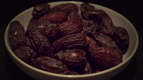 Nutritious Medjool dates in bowl rotating on dark background, close up