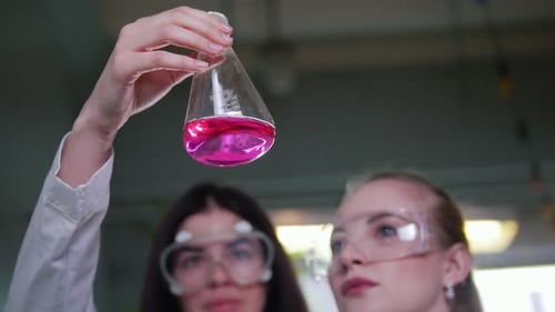 Two Young Women in Chemical Lab Looking at the Flask