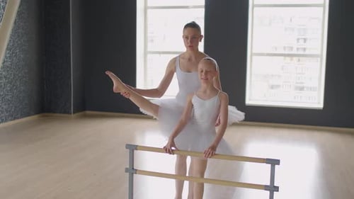 Ballerina Stretching Girls Leg at Training in Dance Studio